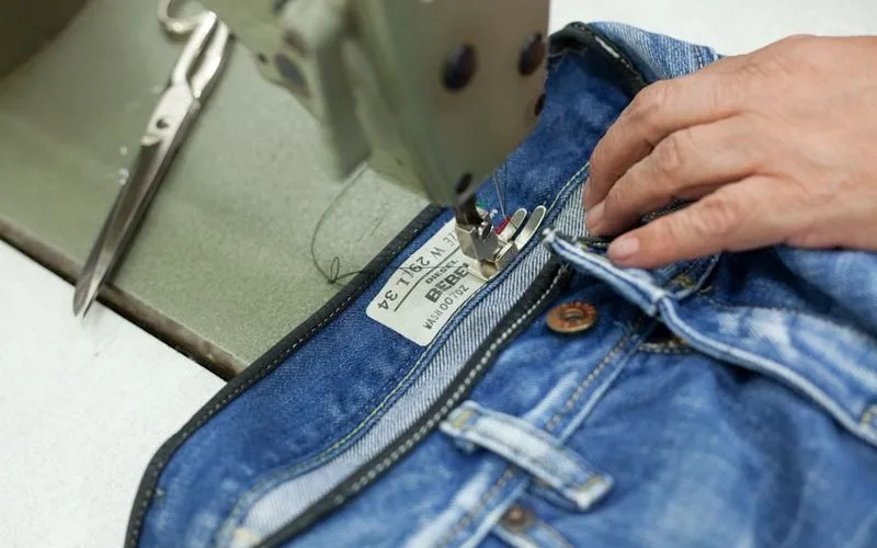 Costureira ajustando calça jeans na máquina de costura